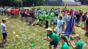 Teams enthusiastically competing in a relay race during the Outrageous Games team building event, surrounded by a crowd of cheering participants.