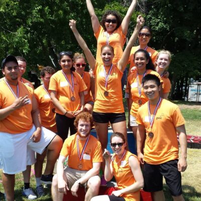 A winning team celebrates their victory at an Outrageous Games team building event, wearing matching orange shirts and medals.