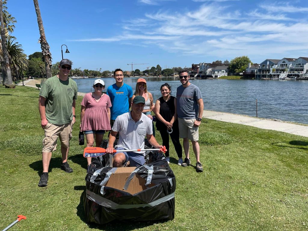 Team standing beside their creatively built cardboard boat during the Build-A-Boat team building event by the lake.