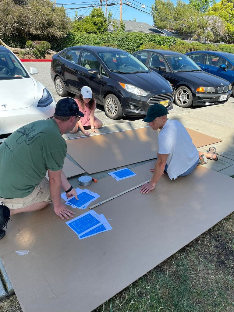 Team members laying out blueprints and cutting cardboard during the Build-A-Boat team building activity.