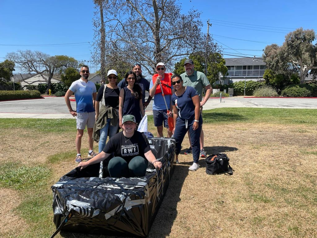 Smiling team showcasing their completed cardboard boat on a sunny day during the Build-A-Boat team building activity.