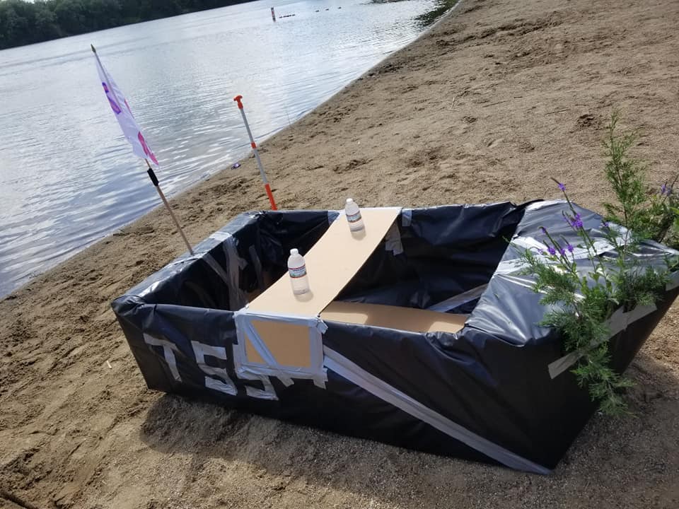 A creatively designed cardboard boat on the shore, ready for the Build-A-Boat team building challenge.