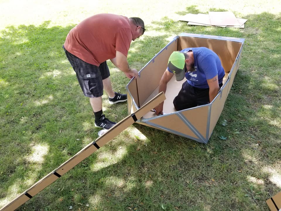 Two participants constructing a cardboard boat outdoors during a Build-A-Boat team building challenge.