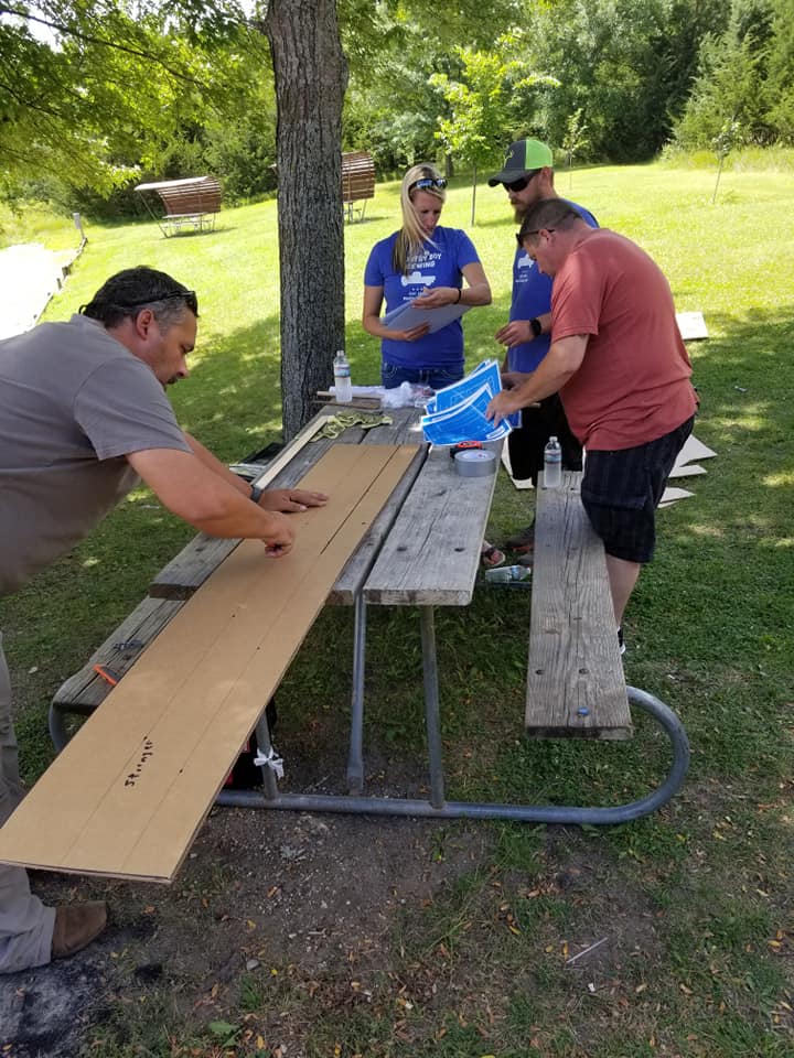 Participants cutting and preparing cardboard pieces for the Build-A-Boat team building challenge at an outdoor setting.