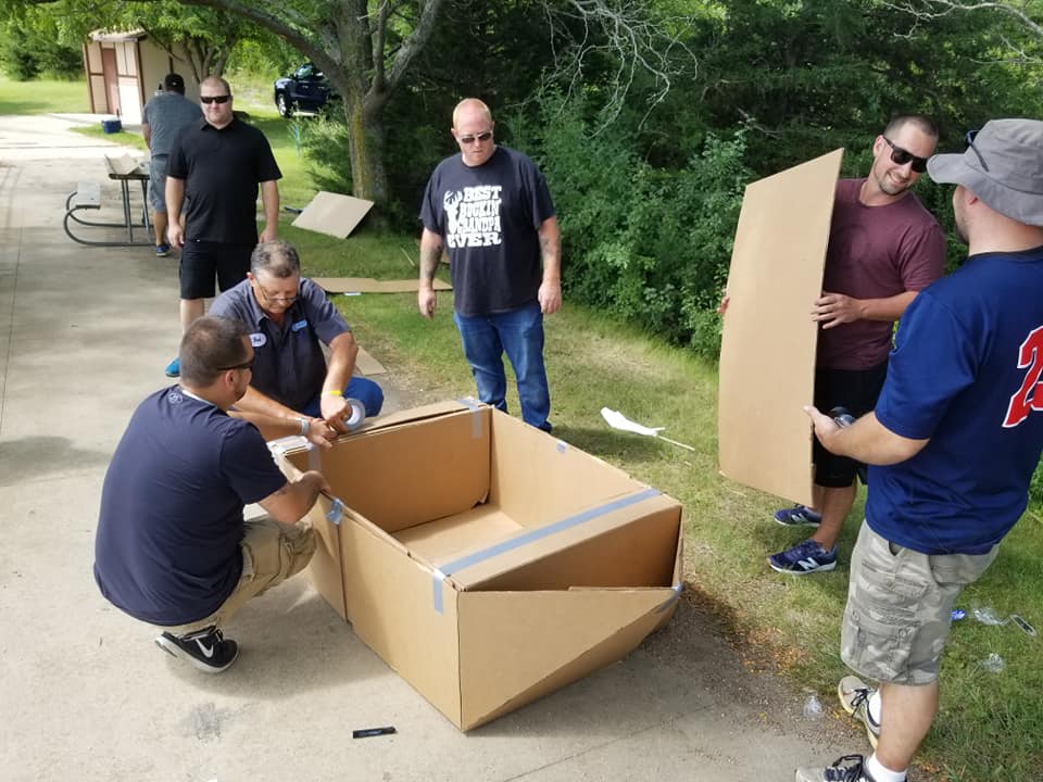 Team members working together to tape and assemble a cardboard boat for the Build-A-Boat team building activity.