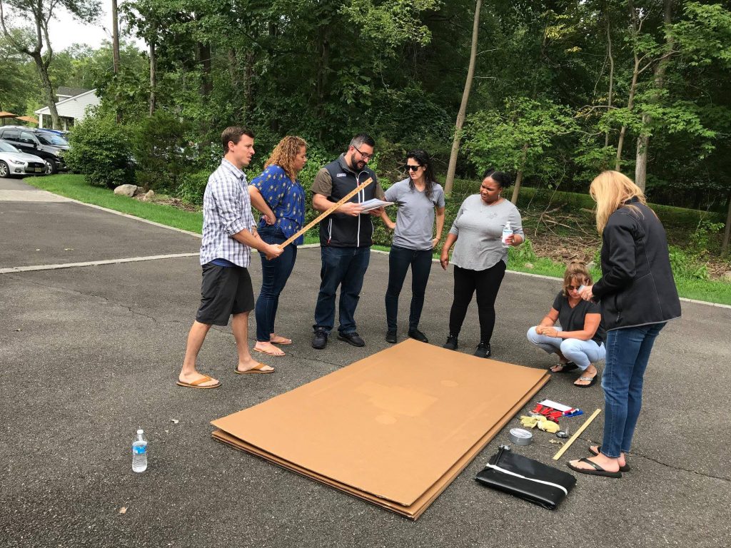 Team brainstorming and planning their cardboard boat design during a Build-A-Boat team building challenge.