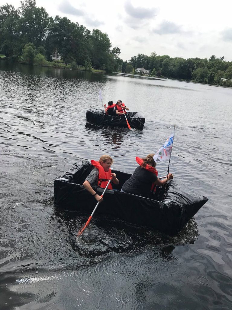 Teams paddling their cardboard boats across the water during the Build-A-Boat team building race.