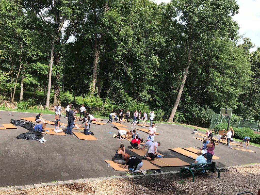 Teams actively working on their cardboard boats during an outdoor Build-A-Boat team building event.