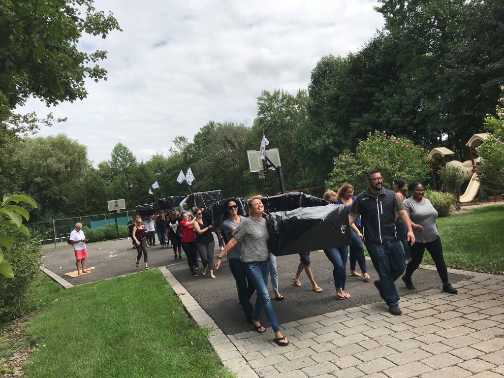 Participants carrying their completed cardboard boats to the water during the Build-A-Boat team building challenge.