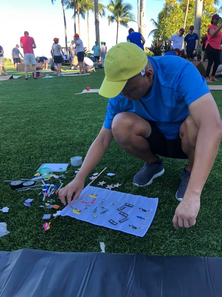 Participant selecting decorative items for their cardboard boat during the Build-A-Boat team building activity on a grassy lawn.