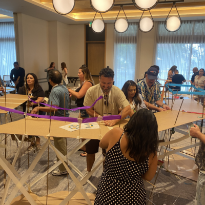 Teams work together to build a large bridge structure using cardboard and colorful materials during the Bridging the Divide team building activity.