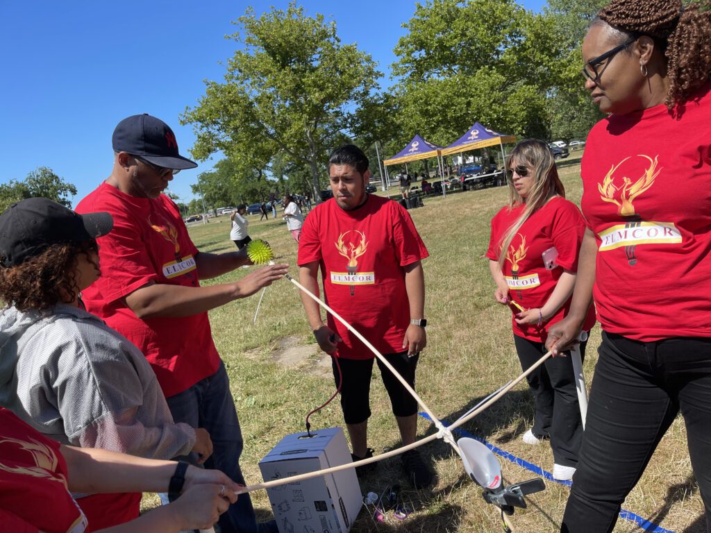 A team of participants in red shirts working together outdoors on constructing a catapult during the Catapult to Success team building activity, showcasing collaboration, creativity, and strategic planning.