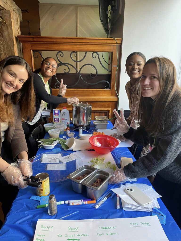 Group of participants smiling while preparing ingredients for the Wicked Good Chowda Cook-Off team building event.