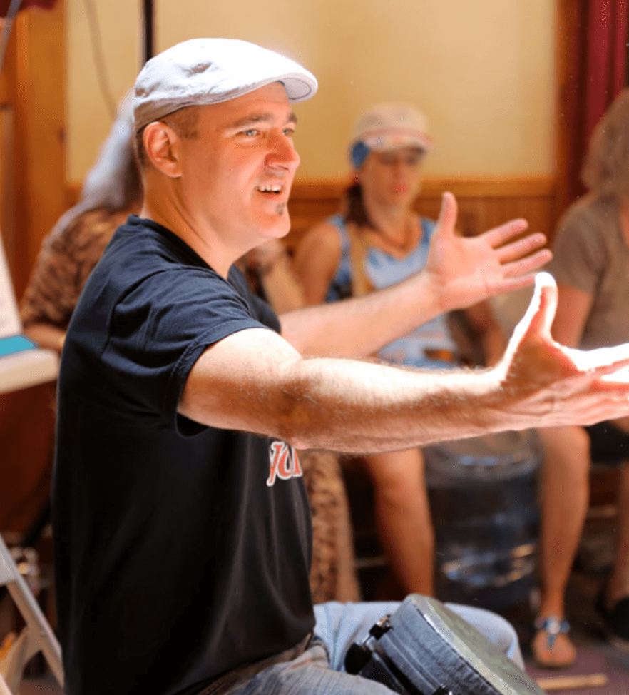 A facilitator leads the Drumming Up A Team event, encouraging participants to connect through rhythm and teamwork, with a vibrant and engaging group dynamic.