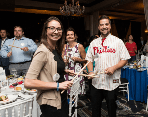 Participants in the Drumming Up A Team event enthusiastically engage in a percussion activity, fostering unity and teamwork while creating an upbeat atmosphere of collaboration and celebration.