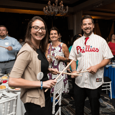 Participants in the Drumming Up A Team event enthusiastically engage in a percussion activity, fostering unity and teamwork while creating an upbeat atmosphere of collaboration and celebration.