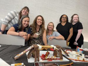 A group of six participants posing proudly behind their chocolate bridge creation during The Chocolate Challenge team building event. The edible bridge is constructed with candy and chocolate materials, showcasing their teamwork and creativity.