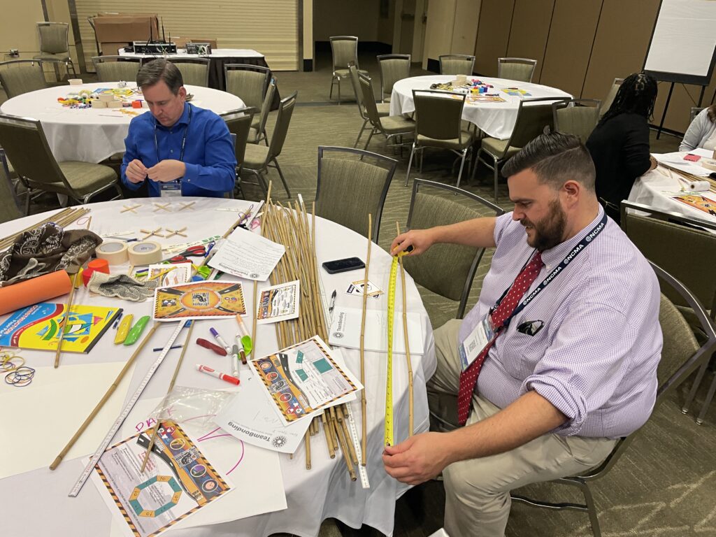 Two participants measure materials and work together to plan their bridge during the Bridging the Divide team building activity.