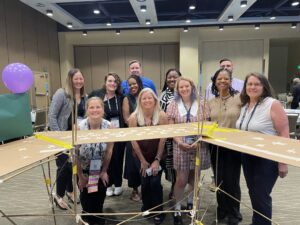 A team poses proudly behind their completed bridge structure during the Bridging the Divide team building activity.