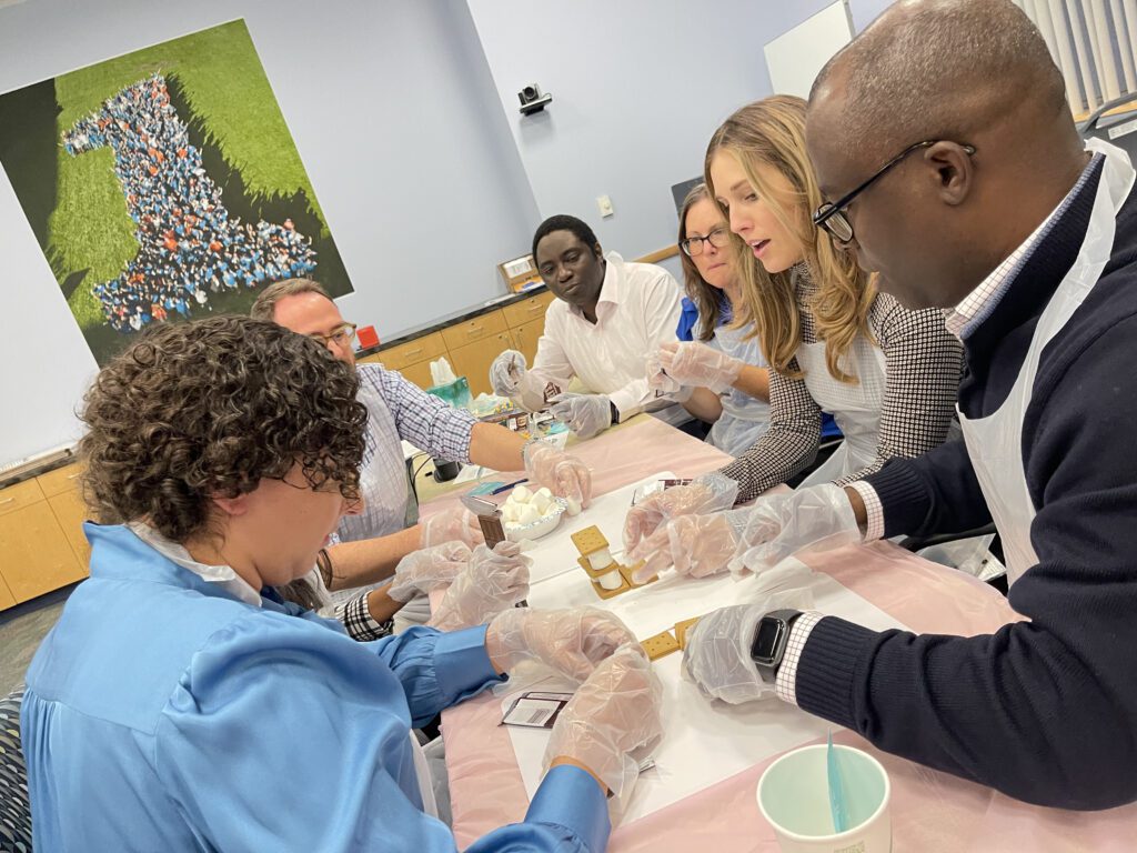 Team members work together during The Chocolate Challenge team building event, wearing gloves and focusing on constructing their project using chocolate materials.