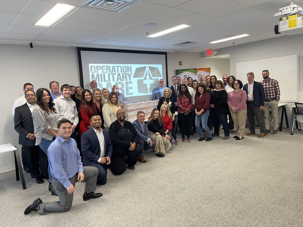 Group photo of participants after completing their Operation Military Care team building event, with care packages ready to be sent to U.S. troops.