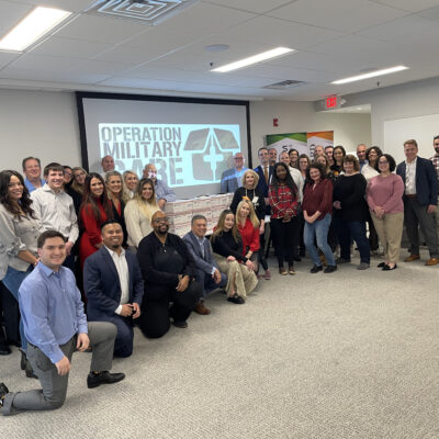 Group photo of participants after completing their Operation Military Care team building event, with care packages ready to be sent to U.S. troops.