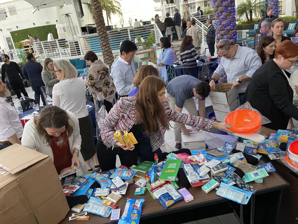 Participants enthusiastically packing care packages for troops during an outdoor Operation Military Care team building event.