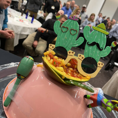 A festive salsa presentation featuring a bowl of fresh salsa garnished with playful cactus-shaped glasses, maracas, and a mini piñata, capturing the lively spirit of the Salsa Showdown team building event.