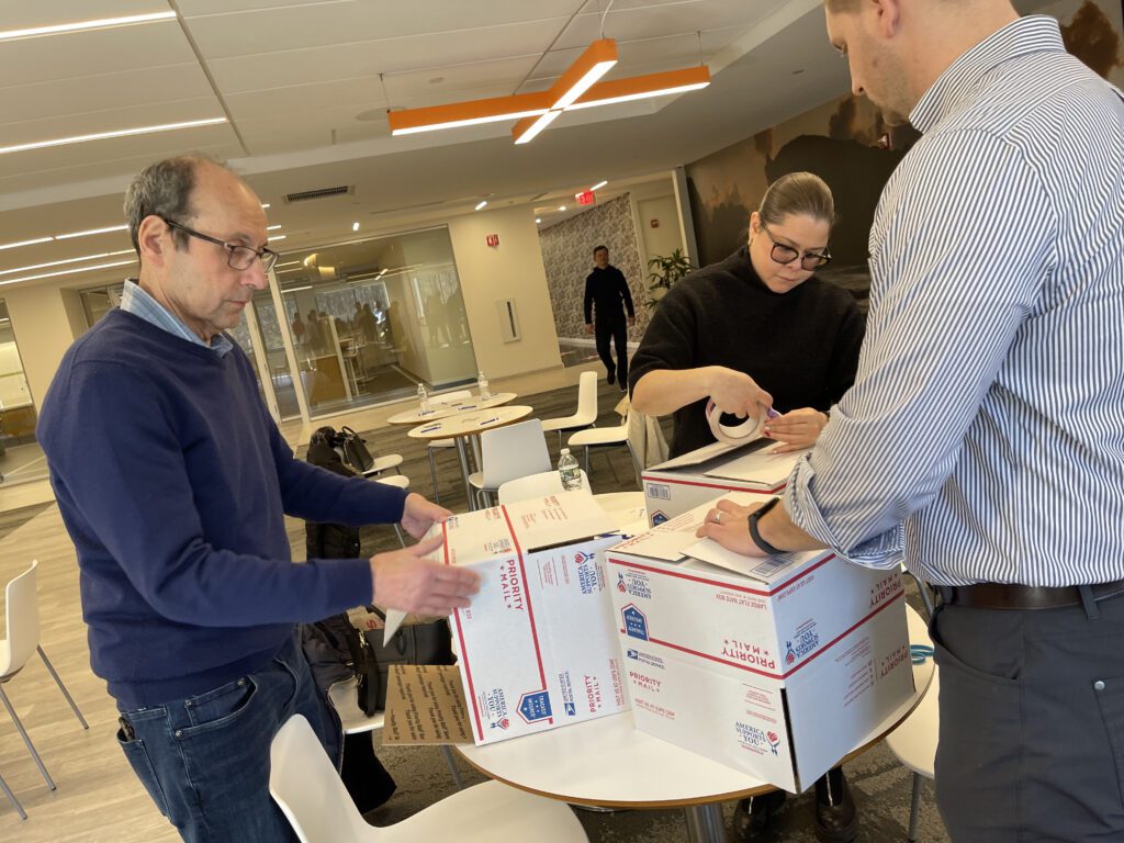 Corporate volunteers sealing care packages for military personnel during an Operation Military Care team building event.