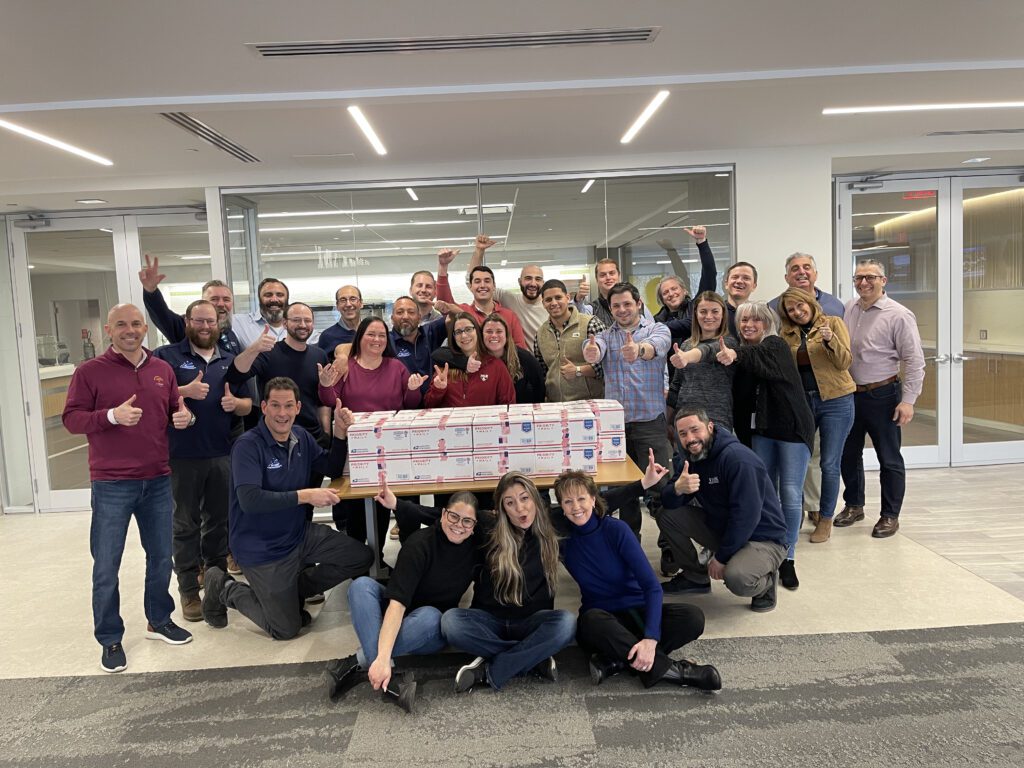 Team poses with completed care packages during the Operation Military Care team building event, ready to be sent to military personnel overseas.