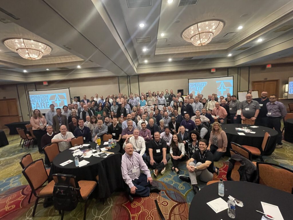 A large group gathers together after successfully completing an Operation Military Care team building event, having packed care packages for U.S. troops.