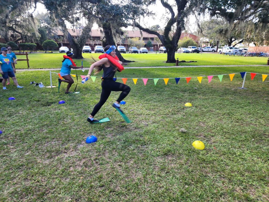 A participant wearing a life vest and flippers runs through an obstacle course during the Outrageous Games team building event, showcasing fun and friendly competition.