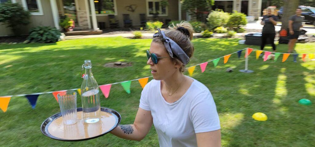 A participant carefully balancing a tray with water and glasses during a relay challenge at the Outrageous Games team building event.