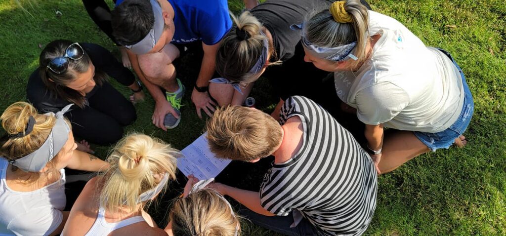 Team huddling together to strategize during a problem-solving challenge at the Outrageous Games team building event.