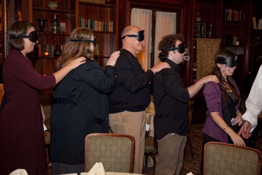 Participants of the Dining in the Dark event forming a human chain while blindfolded, relying on trust and communication as part of a sensory team building experience.