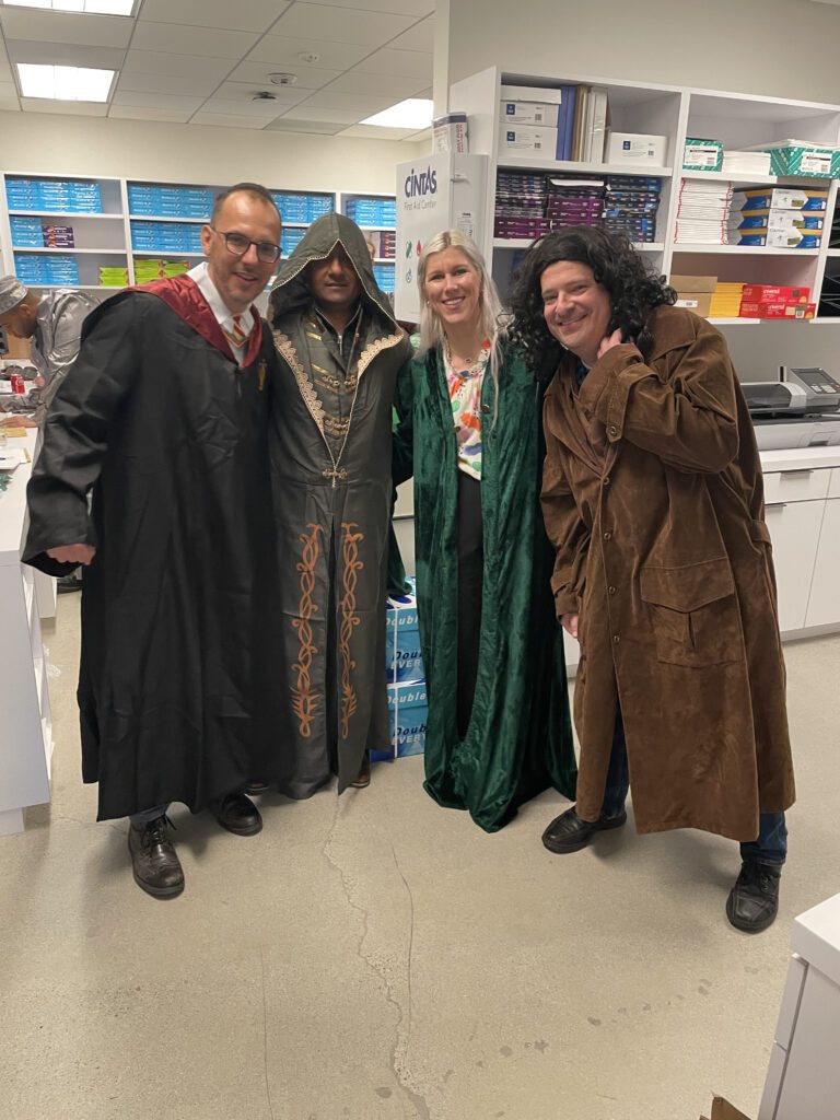 Four participants dressed in various fantasy costumes, including wizard robes and cloaks, pose together during a Custom Team Building event. Their creative outfits reflect the themed nature of the activity.