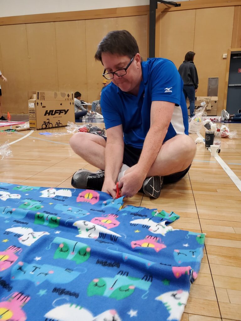 Team member diligently cuts fabric to assemble a fleece blanket during The Big Give charity team building event.