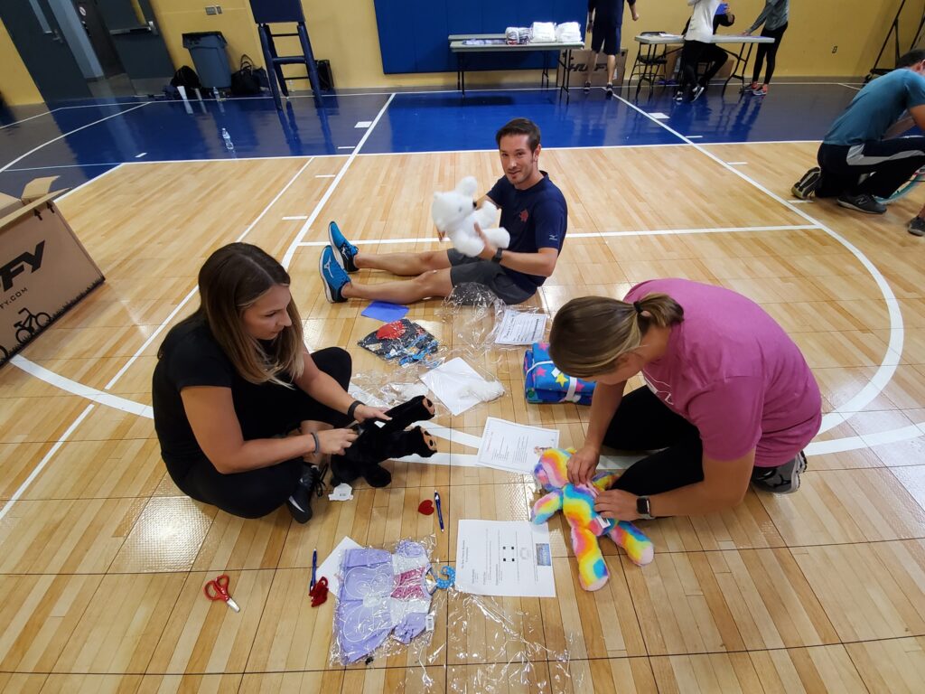 Team members assemble stuffed animals as part of The Big Give charity team building event, preparing toys for donation to children in need.