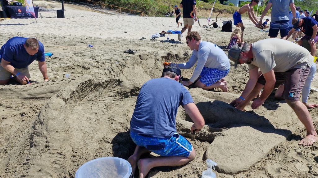 Team members working together to build a sand sculpture at the beach during a fun and collaborative sand sculpting team building event.