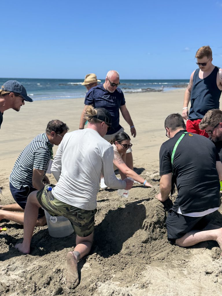 A group of participants collaborating on building a sand sculpture during a sand sculpting team building event at the beach.