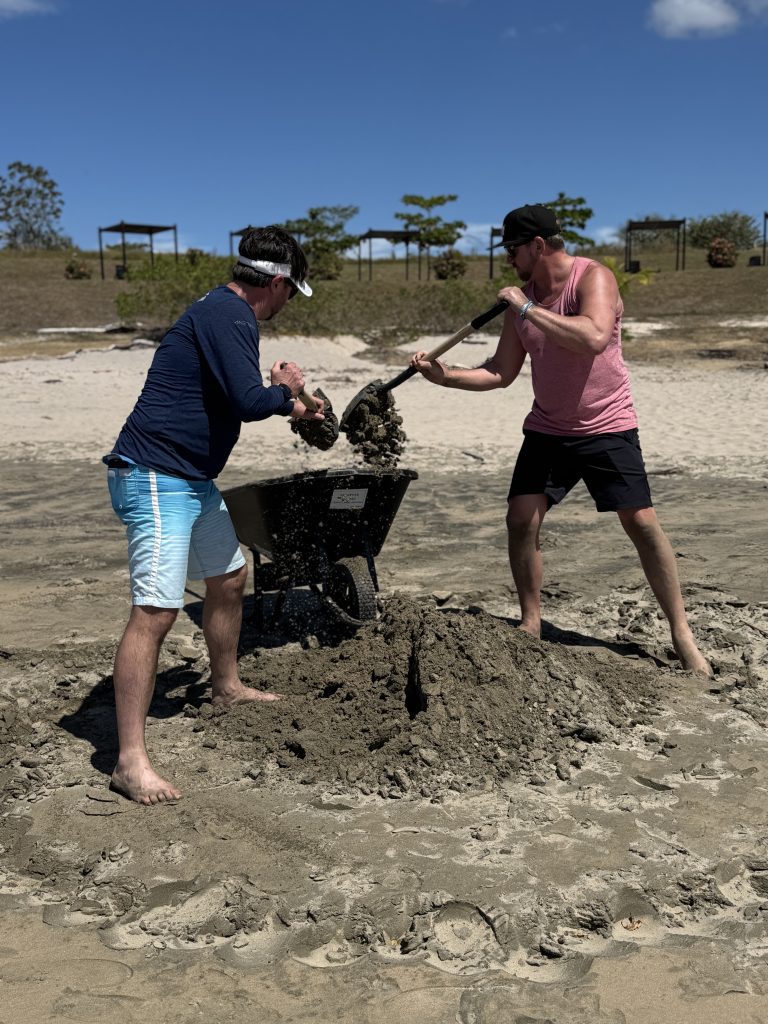 Two team members collaborating to transport sand with a wheelbarrow during a sand sculpting team building event.