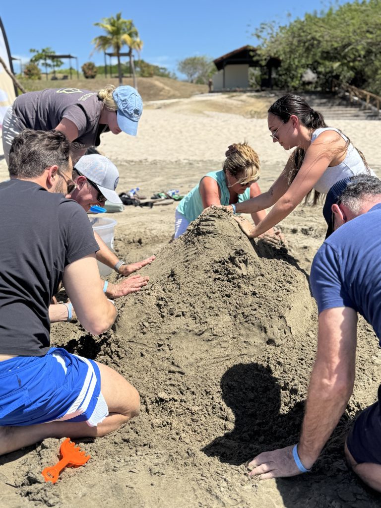 Team members working together to shape a large sand sculpture during a sand sculpting team building event.