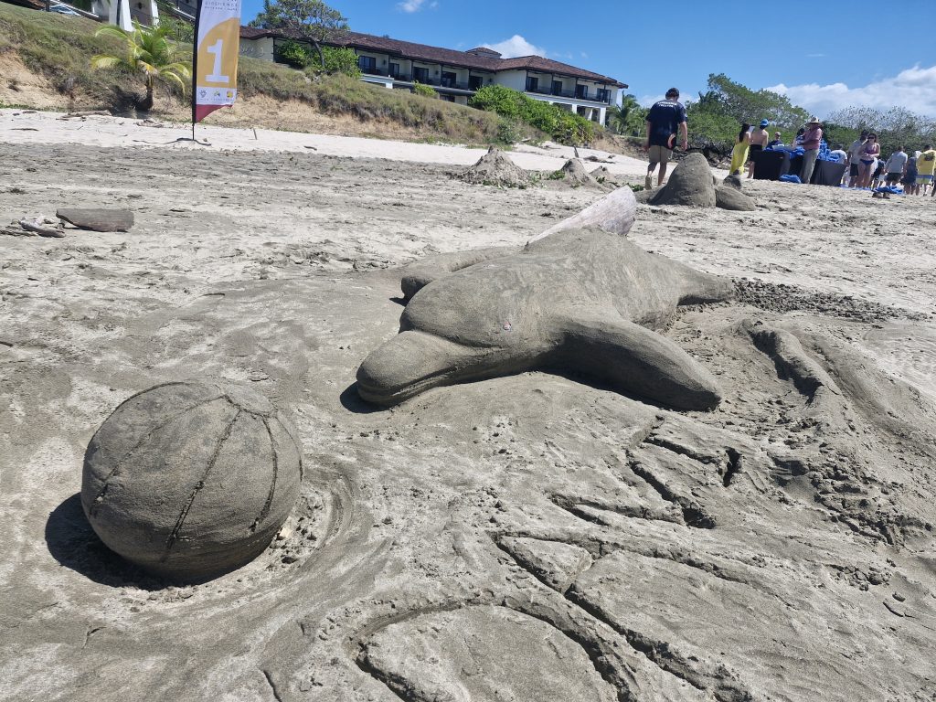 A creative sand sculpture of a dolphin playing with a ball, crafted during a collaborative sand sculpting team building event on the beach.