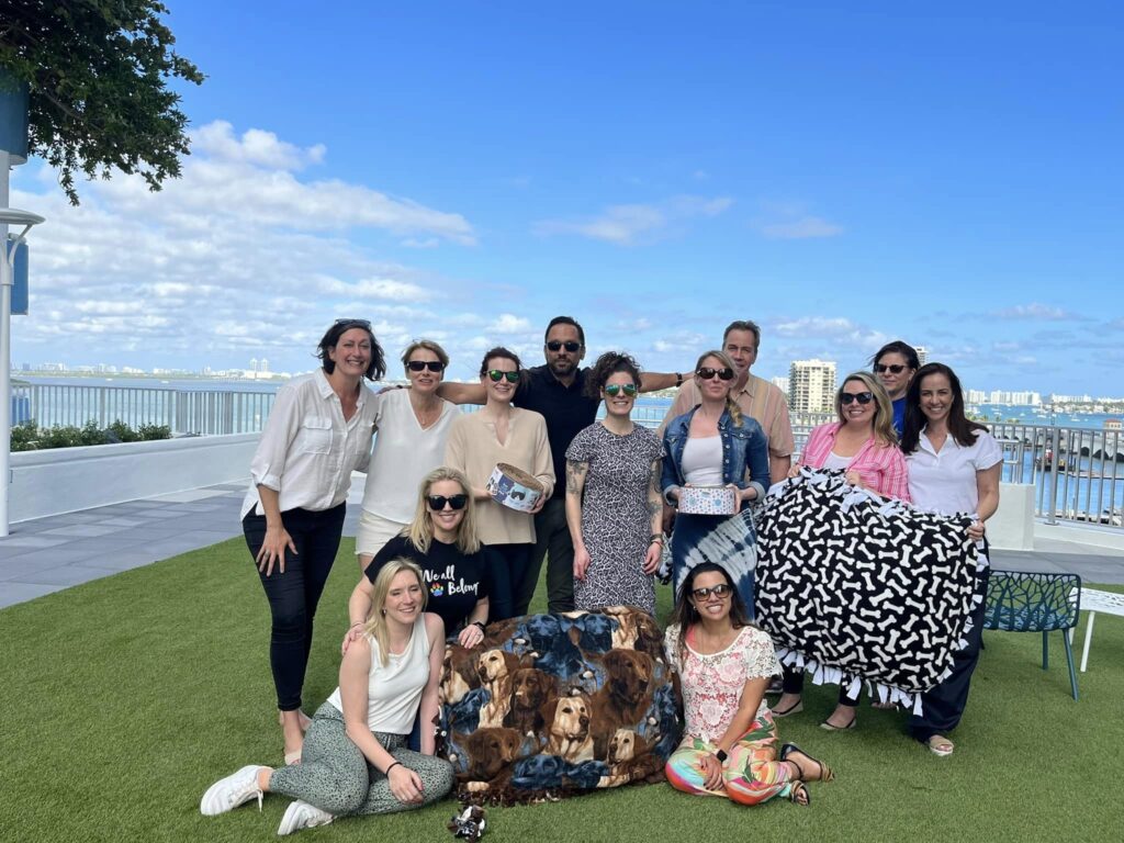 Team members at the Paws For A Cause team building event proudly showcase the colorful dog beds and pull toys they created for donation to a local animal shelter, smiling with a sense of accomplishment.