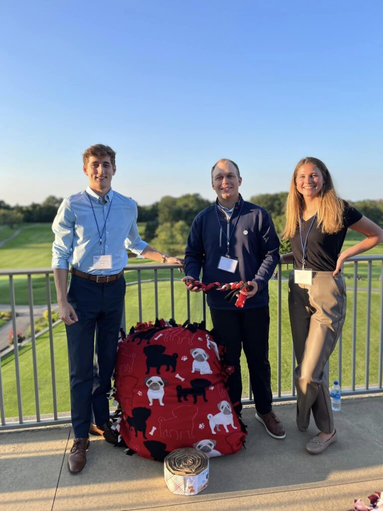 Three participants pose with their completed dog bed and toys during the Paws For A Cause team building event, helping to support local animal shelters.