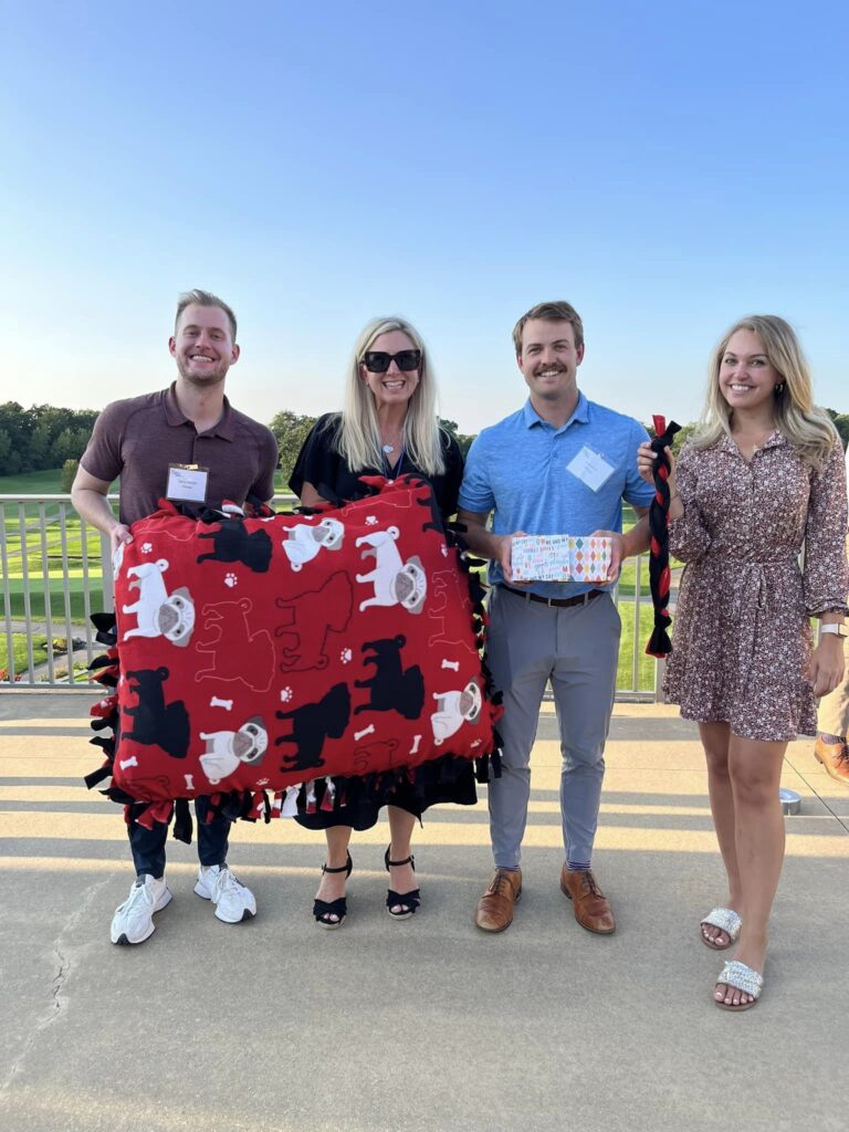 Participants proudly display their handmade dog bed and toys created during the Paws For A Cause team building event, supporting local animal shelters.