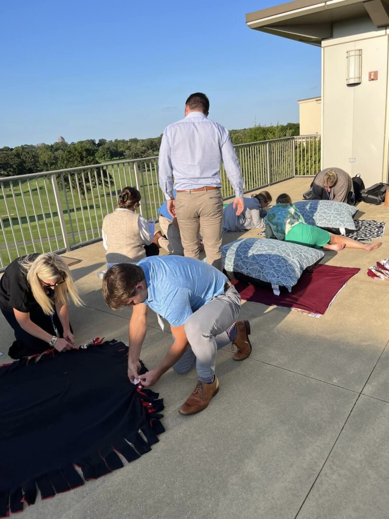 Team members work together outside, crafting dog beds during the Paws For A Cause team building event, supporting animal shelters in need.