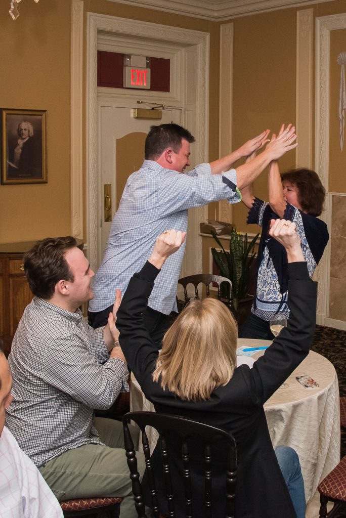 Excited participants raising their hands during a lively Wild Card Team Building Bingo event.