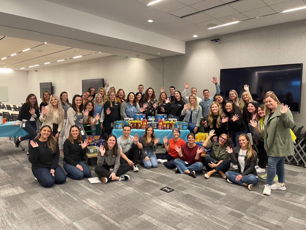 Group of enthusiastic team members posing with collected food donations during the Foodbank Showdown team building event, ready to make a positive impact on their local community.