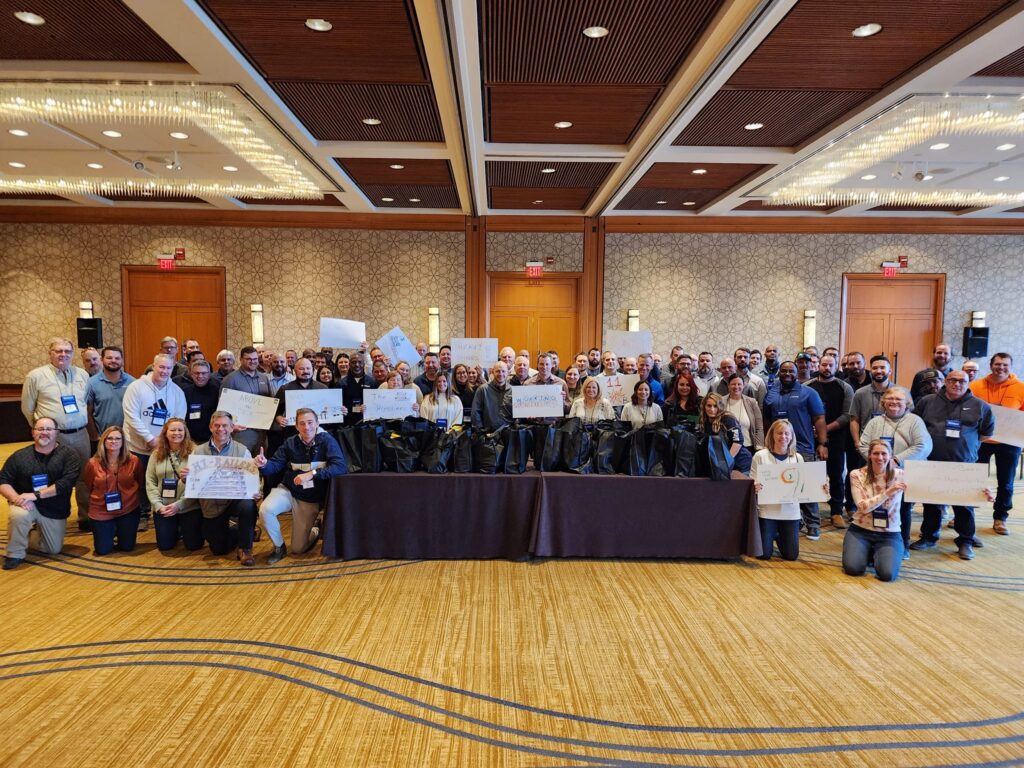 Large group photo from the Foodbank Showdown team building event, where participants proudly display their completed care packages, ready to be donated to families in need through a local charity.